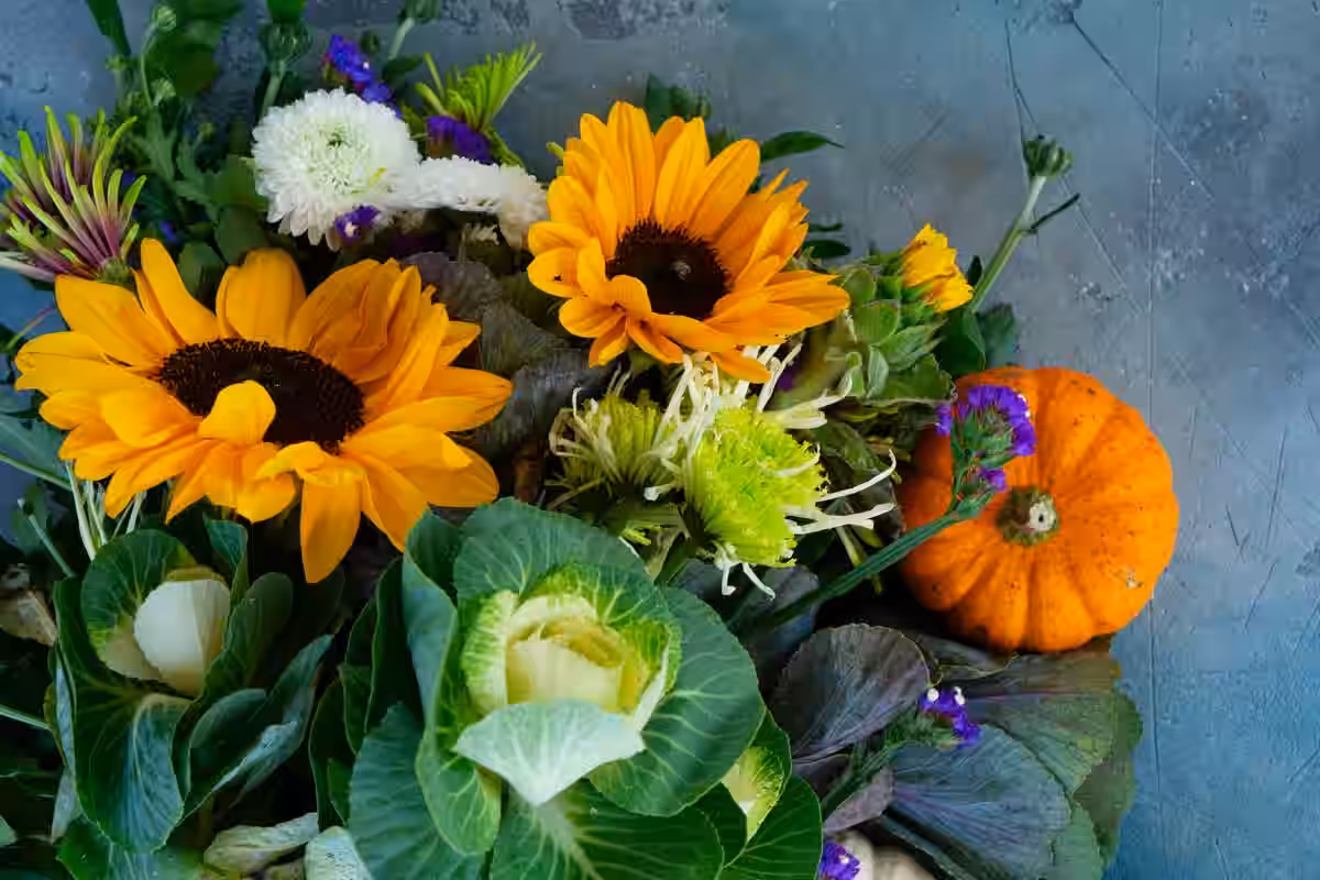 A vibrant bouquet of flowers and fresh vegetables arranged on a blue table, creating a colorful centerpiece.